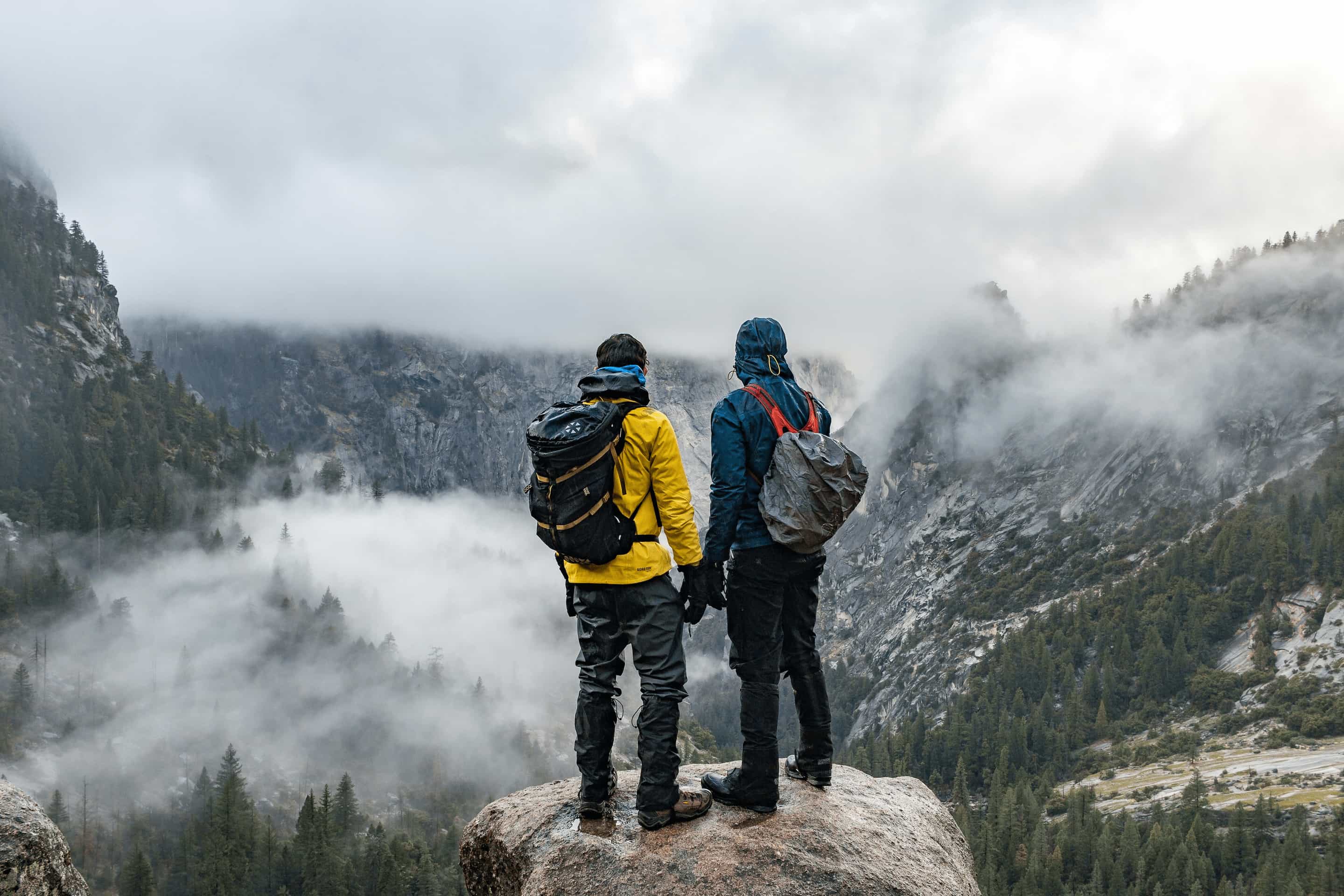 Two people in weatherproof clothing looking out over a misty valley