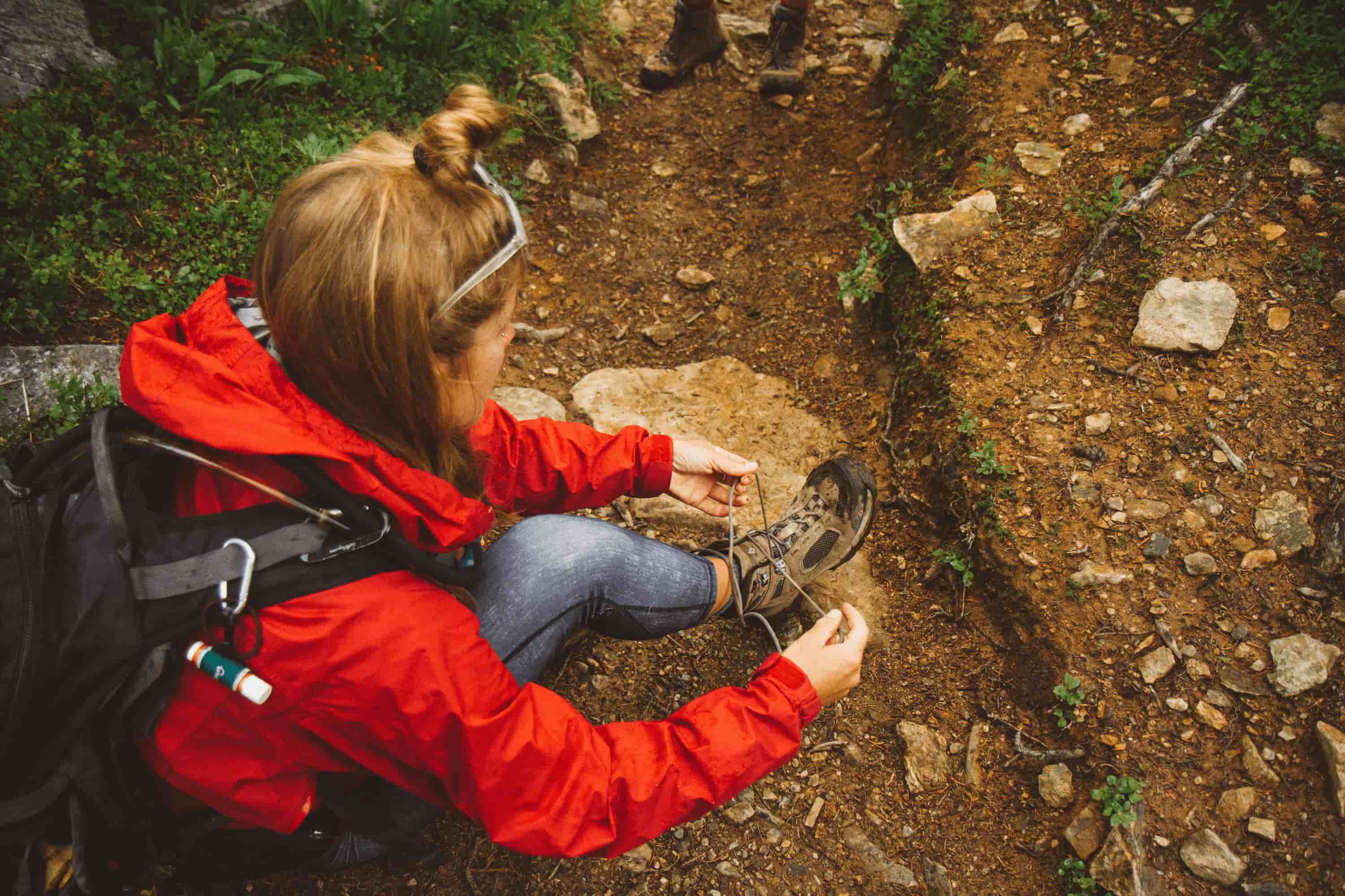 A woman tying her shoe on a rocky trail